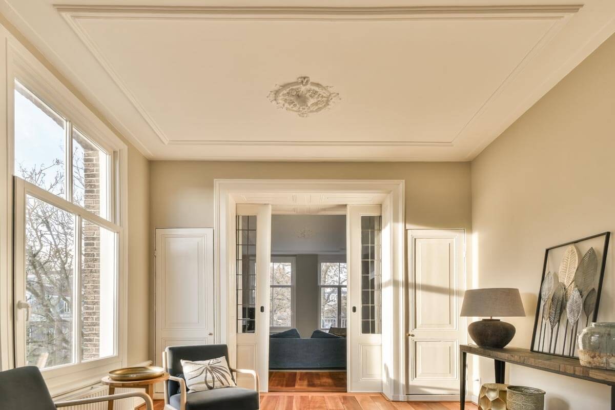 Bright salon with a wide window front, stucco ceiling and a sliding door passage leading through to the rear part of the room.