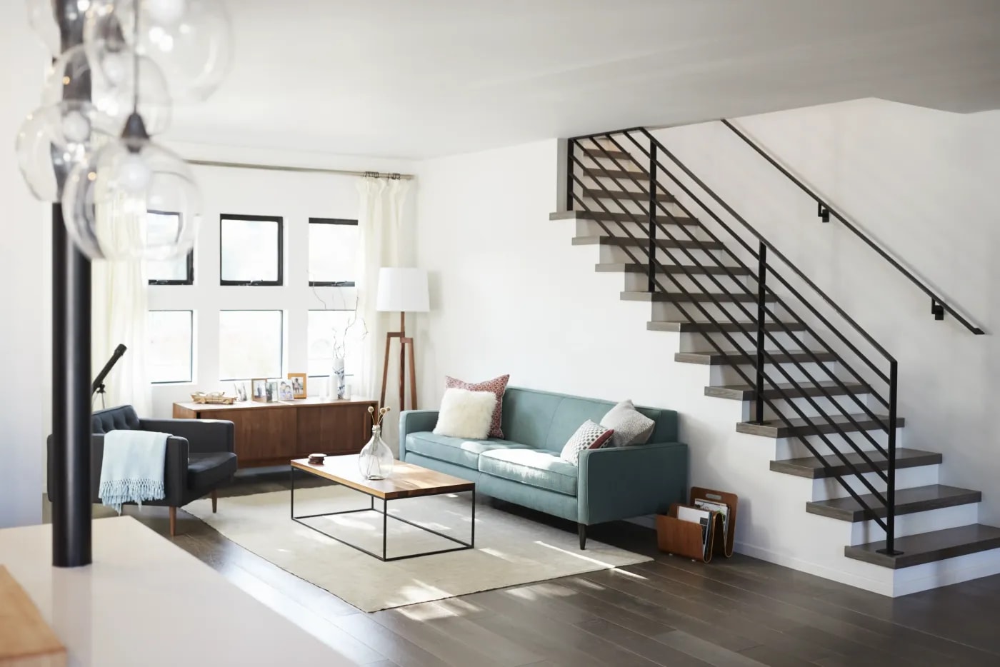 View from the corner of a room into a living room with a modern seating area in front of the side wall with small windows and a staircase to the upper floor along the right wall.