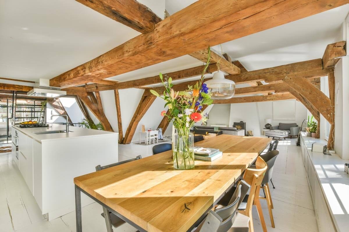 L-shaped room under the roof with partial sloping ceilings and low ceiling height, with tightly arranged furniture including a seating group, sideboards and upholstered furniture in the background.